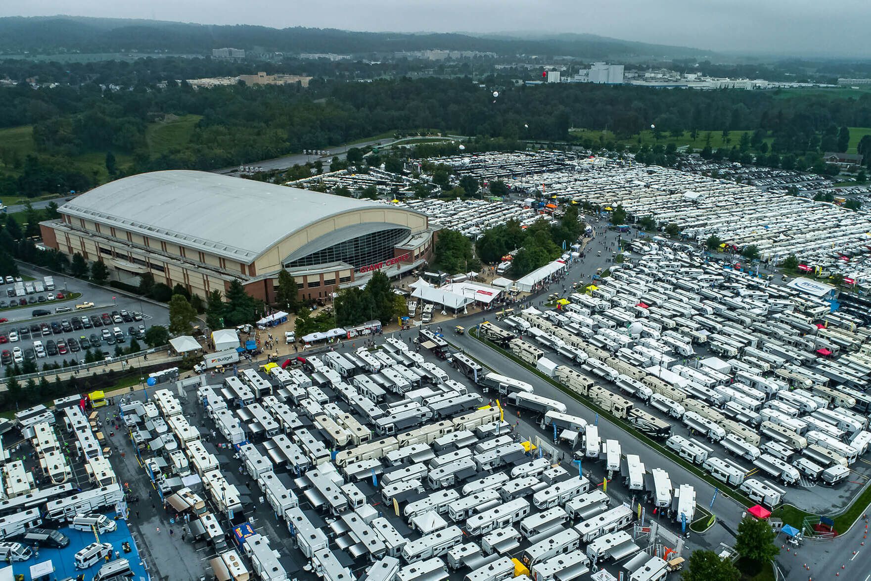 Aerial of America's Largest RV Show, Hershey, Pennsylvania, parking lot filled with RVs in the foreground, exterior of Giant Center, farms and countryside in the background on a cloudy day