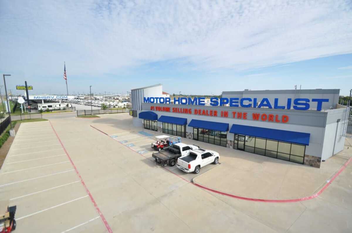 Aerial of front exterior and parking of MHSRV, Alvarado, Texas, RVs for sale in the background, a blue sky with clouds