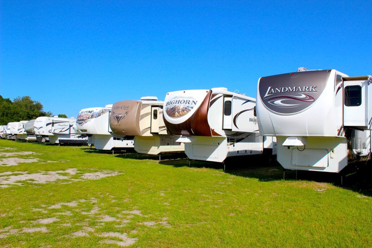 Line of RVs for sale at PPL Motor Homes, Summerfield, Florida, on green grass, trees on the left, a bright blue sky on a sunny day in the background