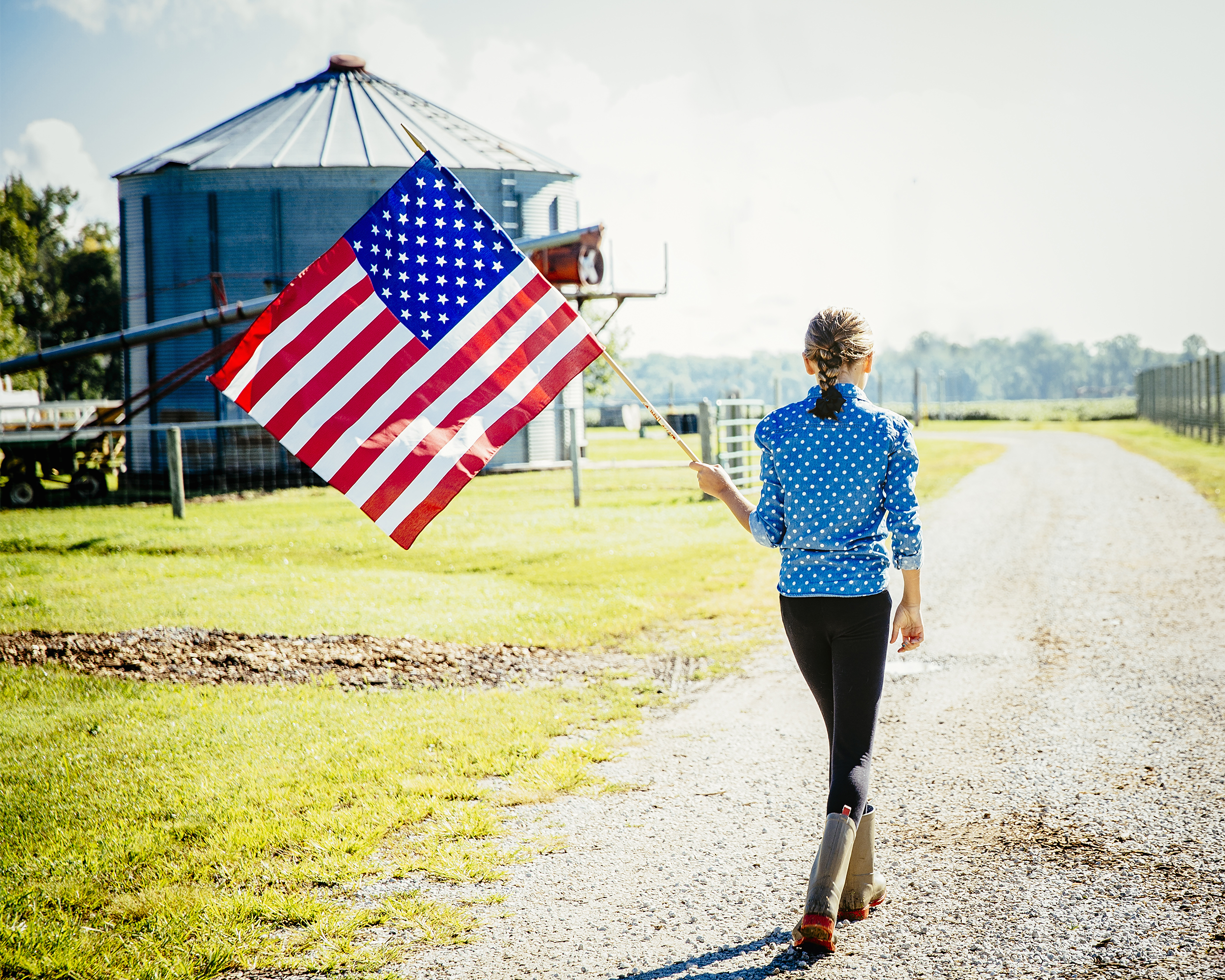 girl walking with American flag in rural area