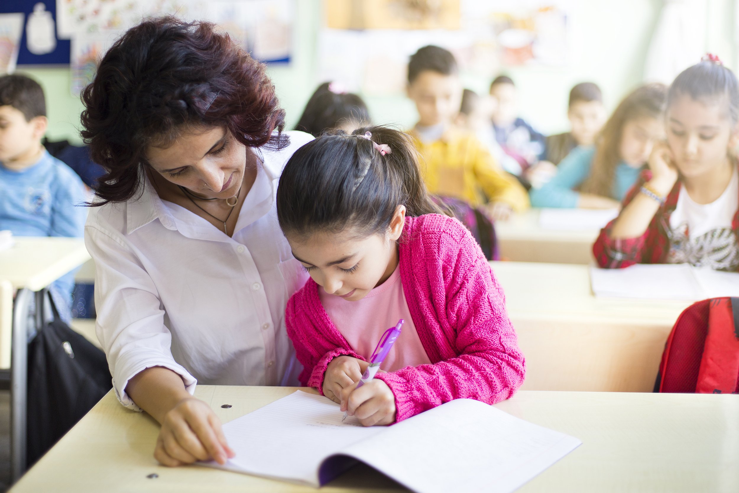 teacher teaches to write to the girl student in the class