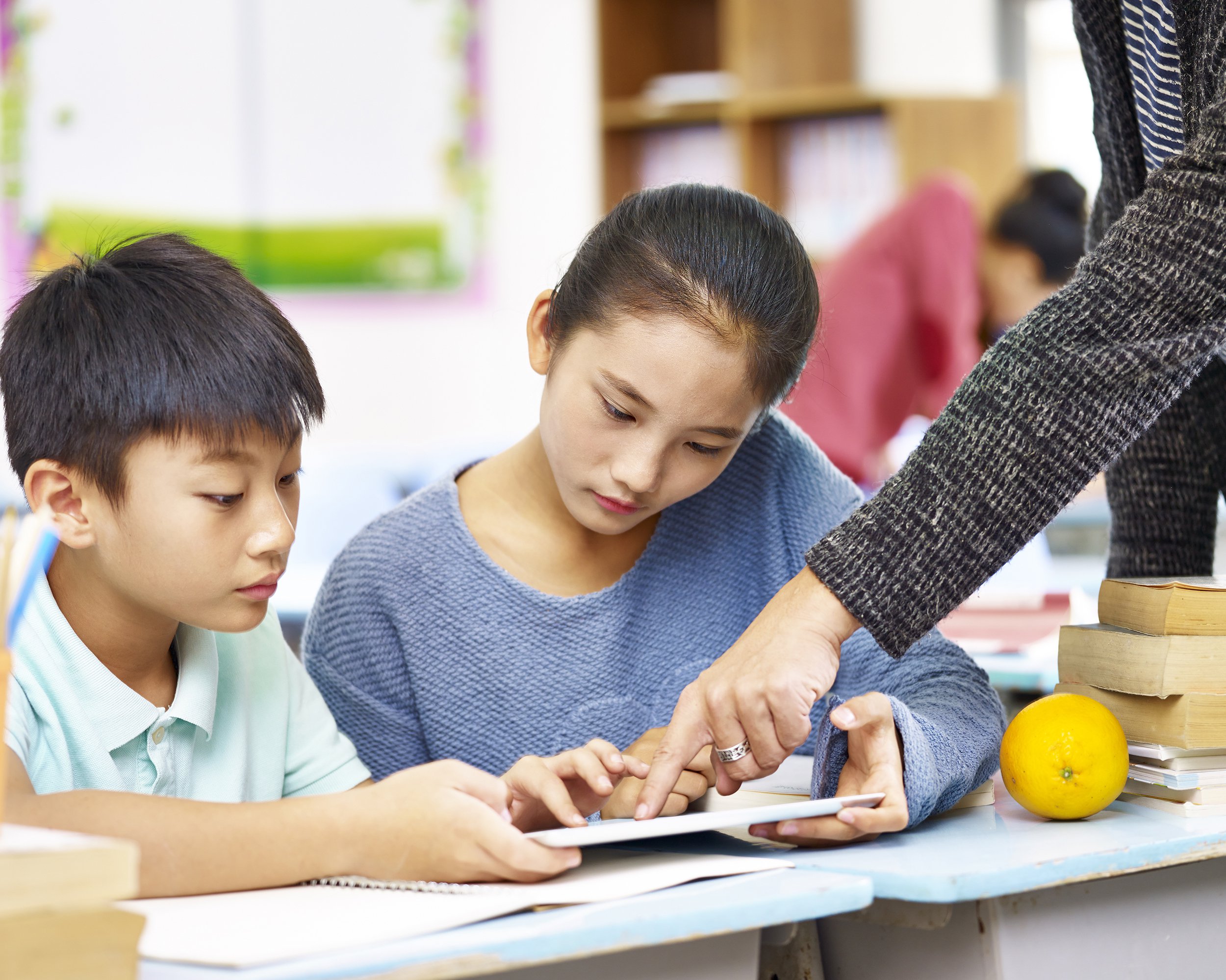 Asian schoolchildren getting help from teacher in class