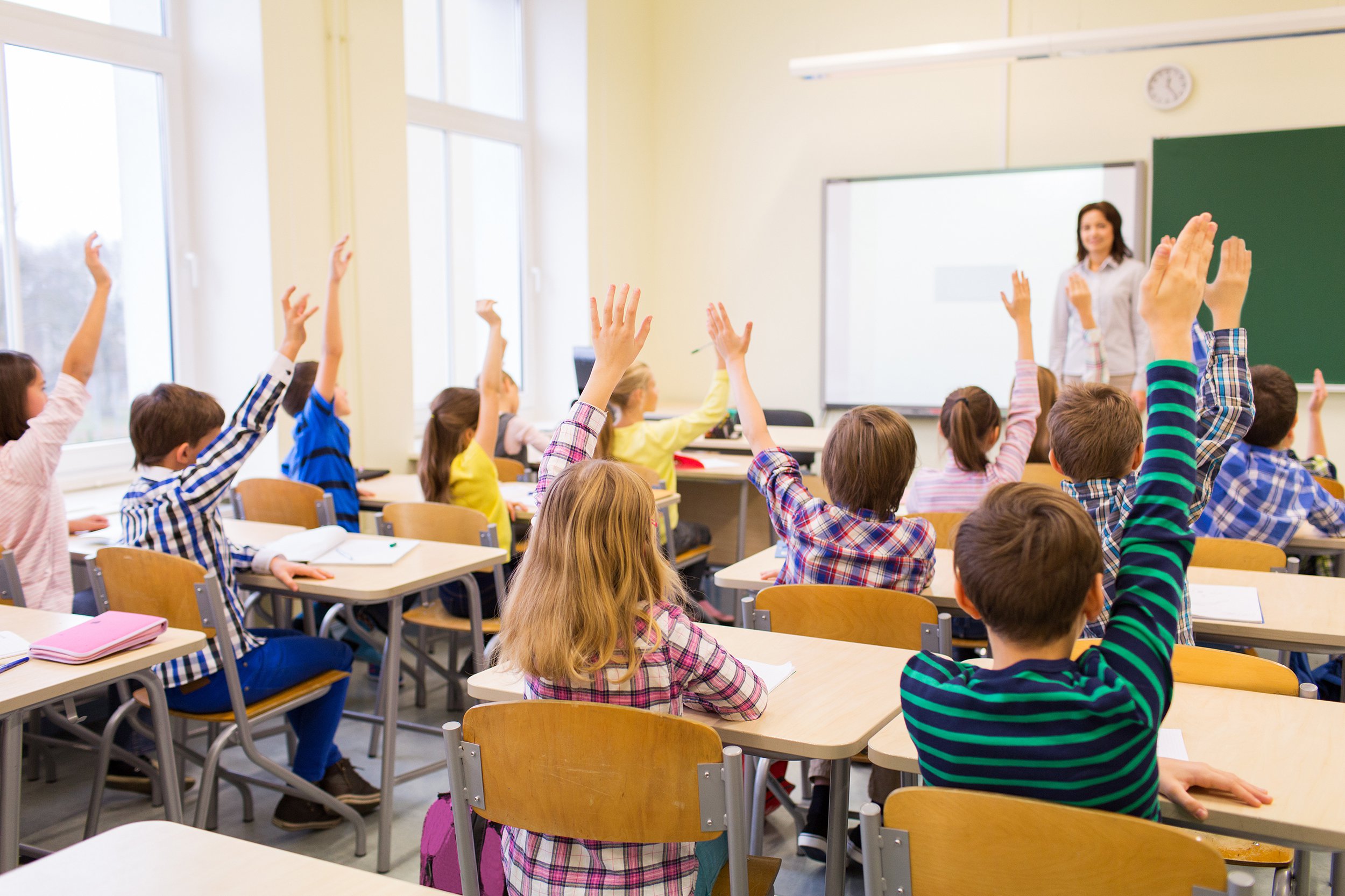 group of school kids raising hands in classroom