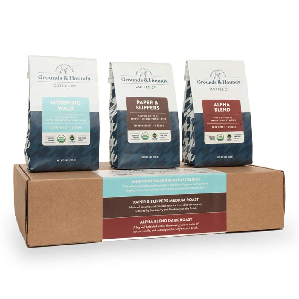 Three bags of Grounds & Hounds Coffee—Morning Walk, Paper & Slippers, and Alpha Blend—are displayed on top of a brown box with matching labels describing each coffee blend.