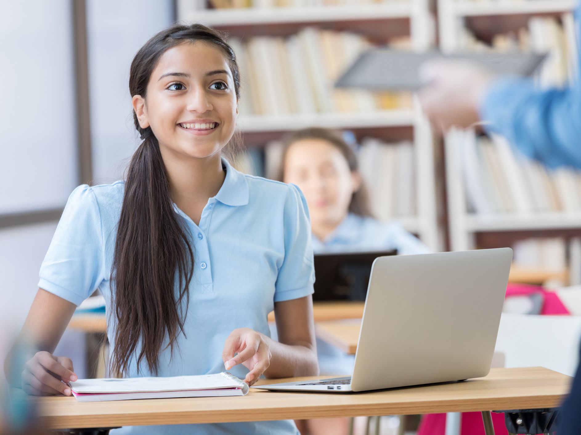 Hispanic teen girl smiling and listening to teacher with computer and notepad.