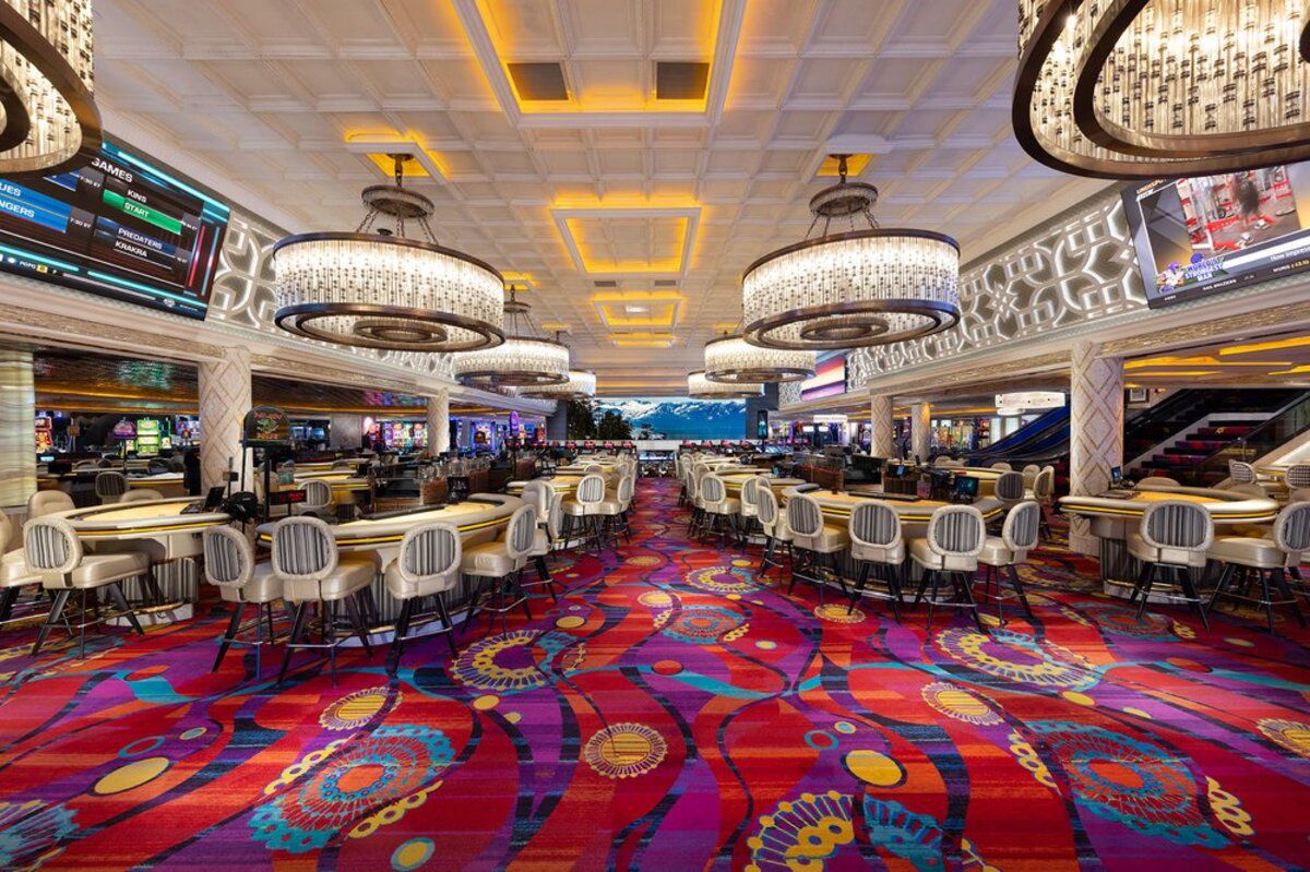 Peppermill Resort Spa Casino, Reno, Nevada, semi-circular game tables with seating, colorful carpet and chandelier lights, slot machines in the distant background