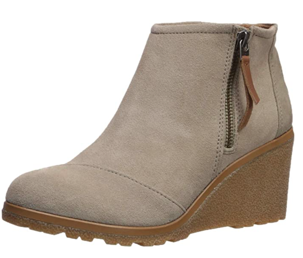 A beige suede ankle boot with a wedge heel, side zipper, and textured rubber sole, designed for casual or semi-formal wear.