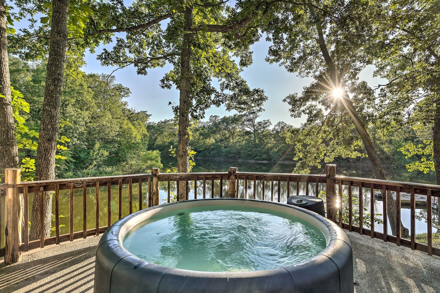 Blow up pool on a deck facing a lake on a summer day with trees filtering sunlight