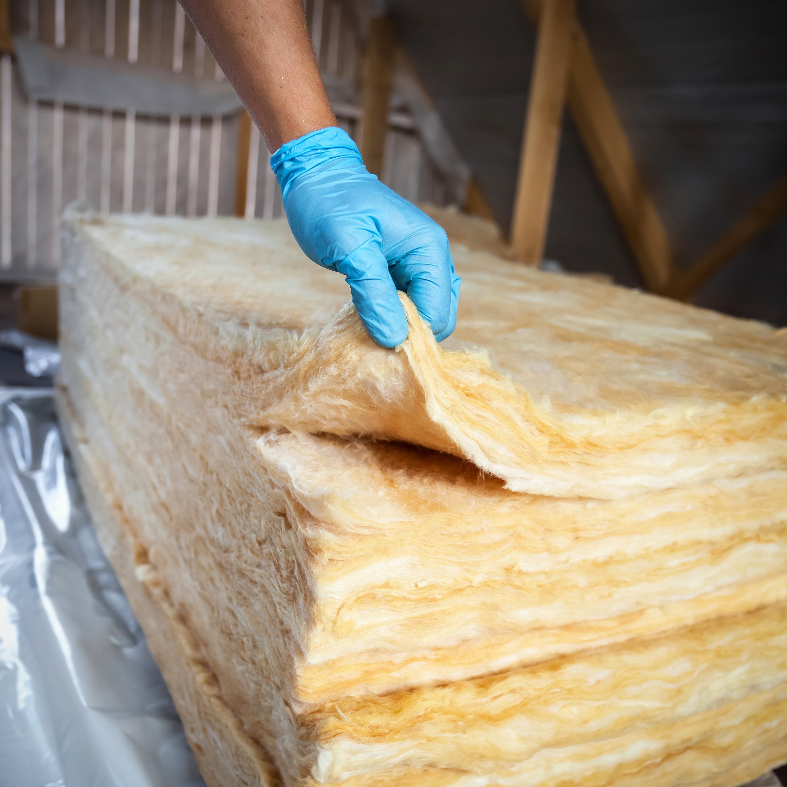 gloved hands holding insulation in attic of house
