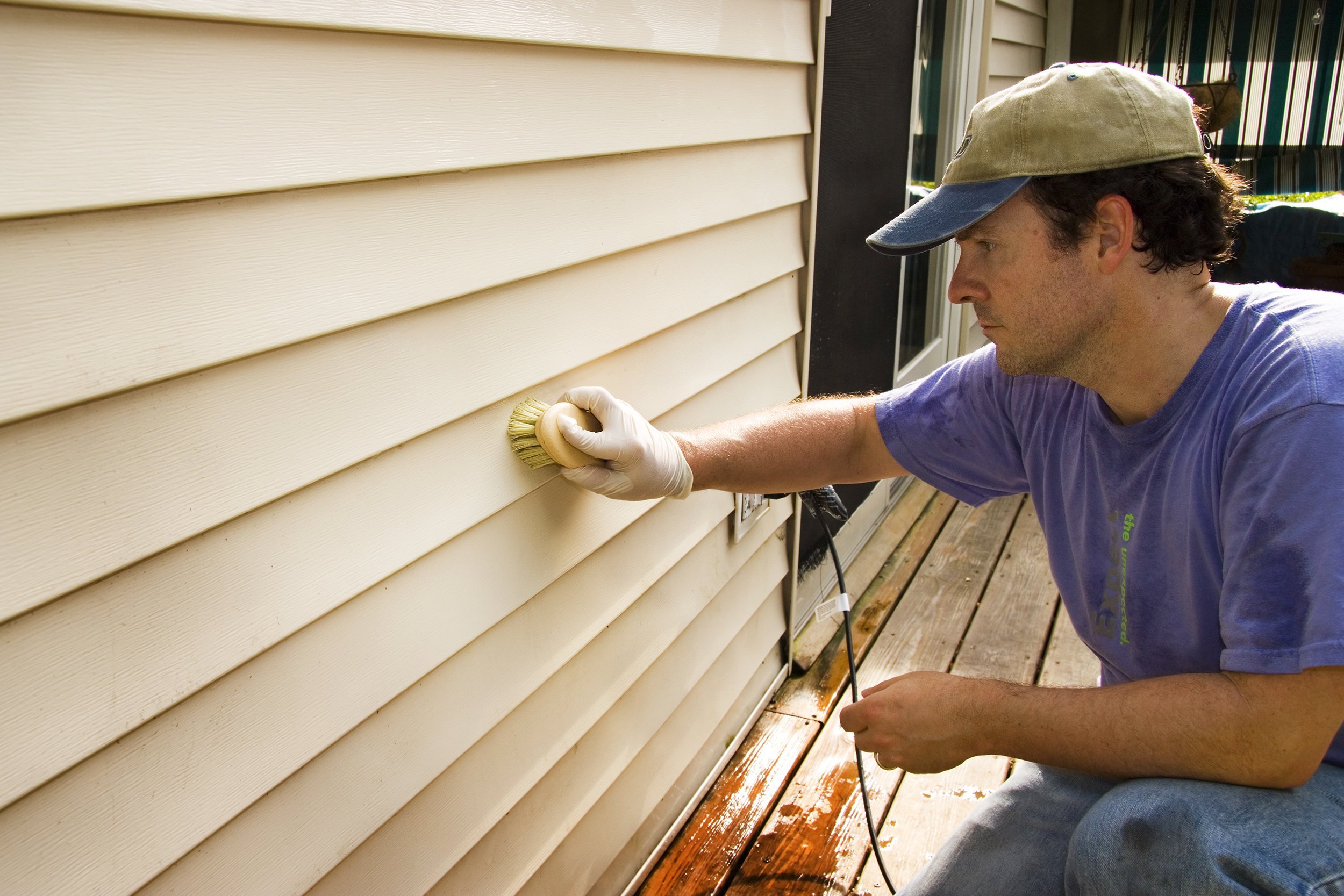man washing vinyl on side of house