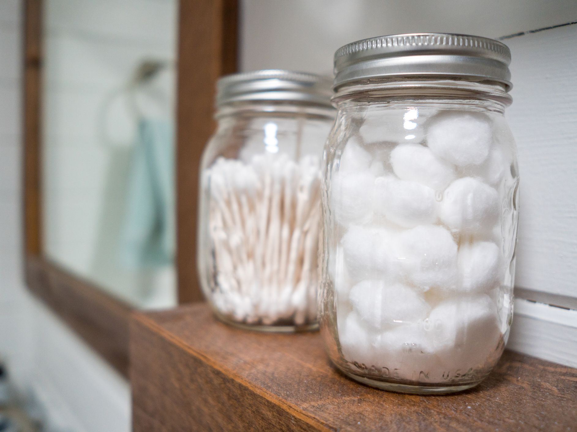 Cotton balls and cotton swabs in mason jars on farmhouse bathroom shelf.