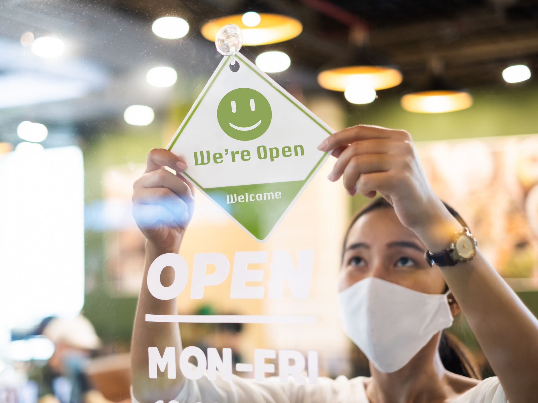 Business owner Asian woman wear protective face mask ppe hanging open sign at her restaurant / café, open again after lock down due to outbreak of coronavirus covid-19