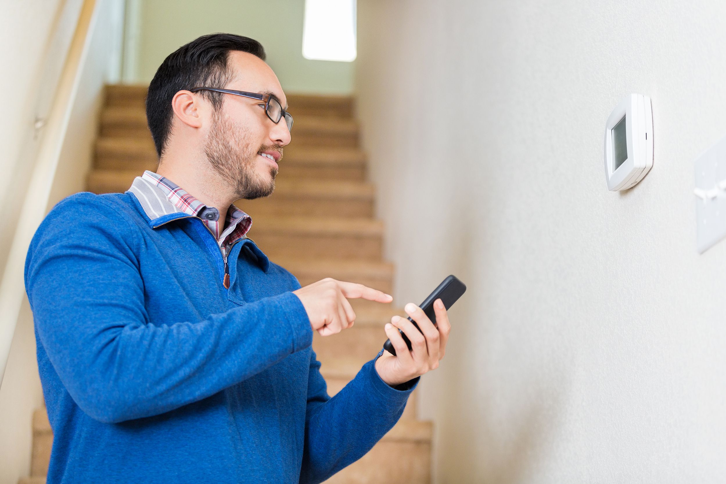 man uses smart phone to control thermostat