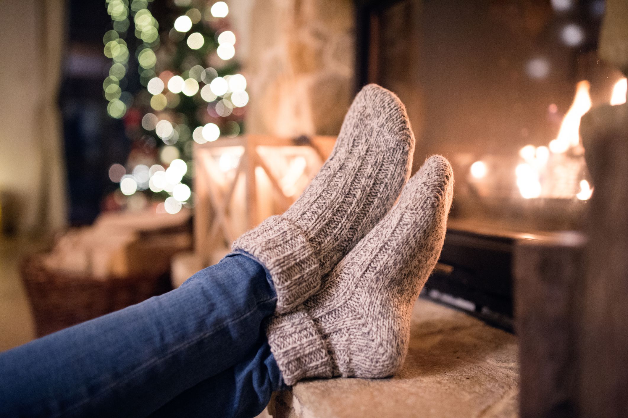 Feet of unrecognizable woman in woollen socks by the Christmas fireplace.