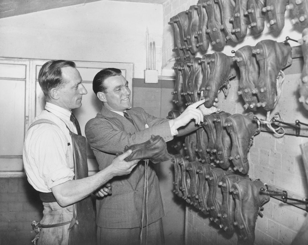 English footballer Eddie Hapgood (1908- 1973), captain of Arsenal F.C., discusses football boots with 'Cobbler' Lee, the team's shoe-maker, at Highbury, London, 22nd December 1937.