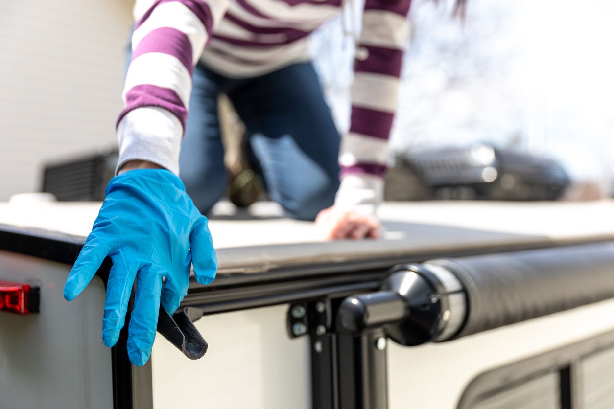 A woman is doing the maintenance of a camper trailer. She is cleaning the gutters so the water evacuates correctly