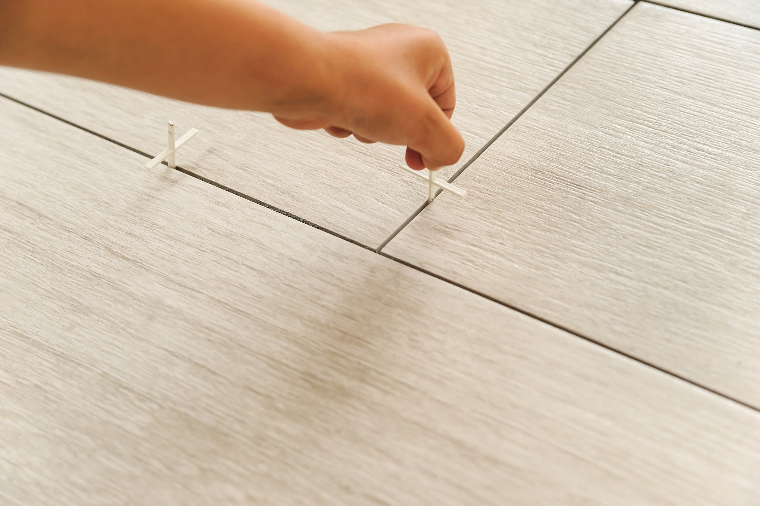 worker sets plastic crosses between the tiles