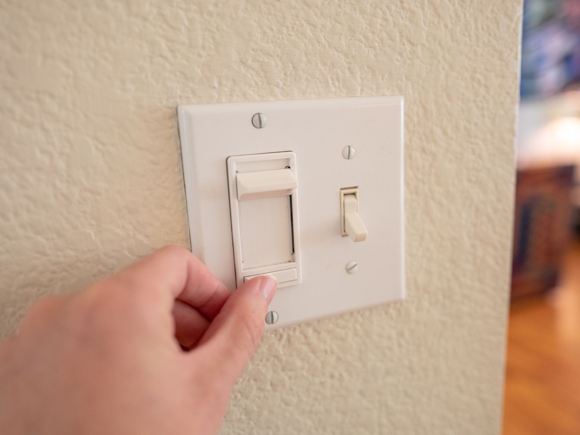 Close-up, personal perspective or point of view of human hand of a man adjusting dimmer switch on wall light switch, September 24, 2019