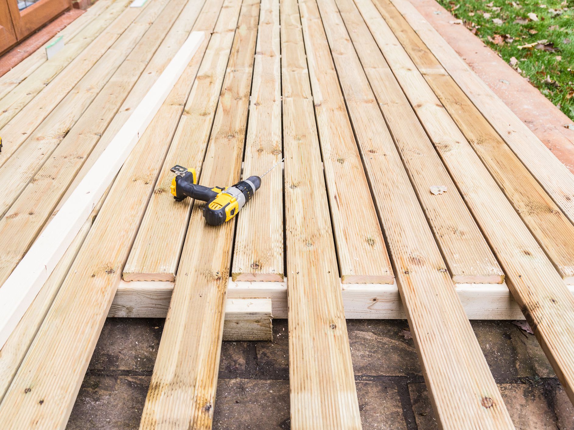 A new wooden, timber deck being constructed. it is partially completed. two drill can be seen on the decking.