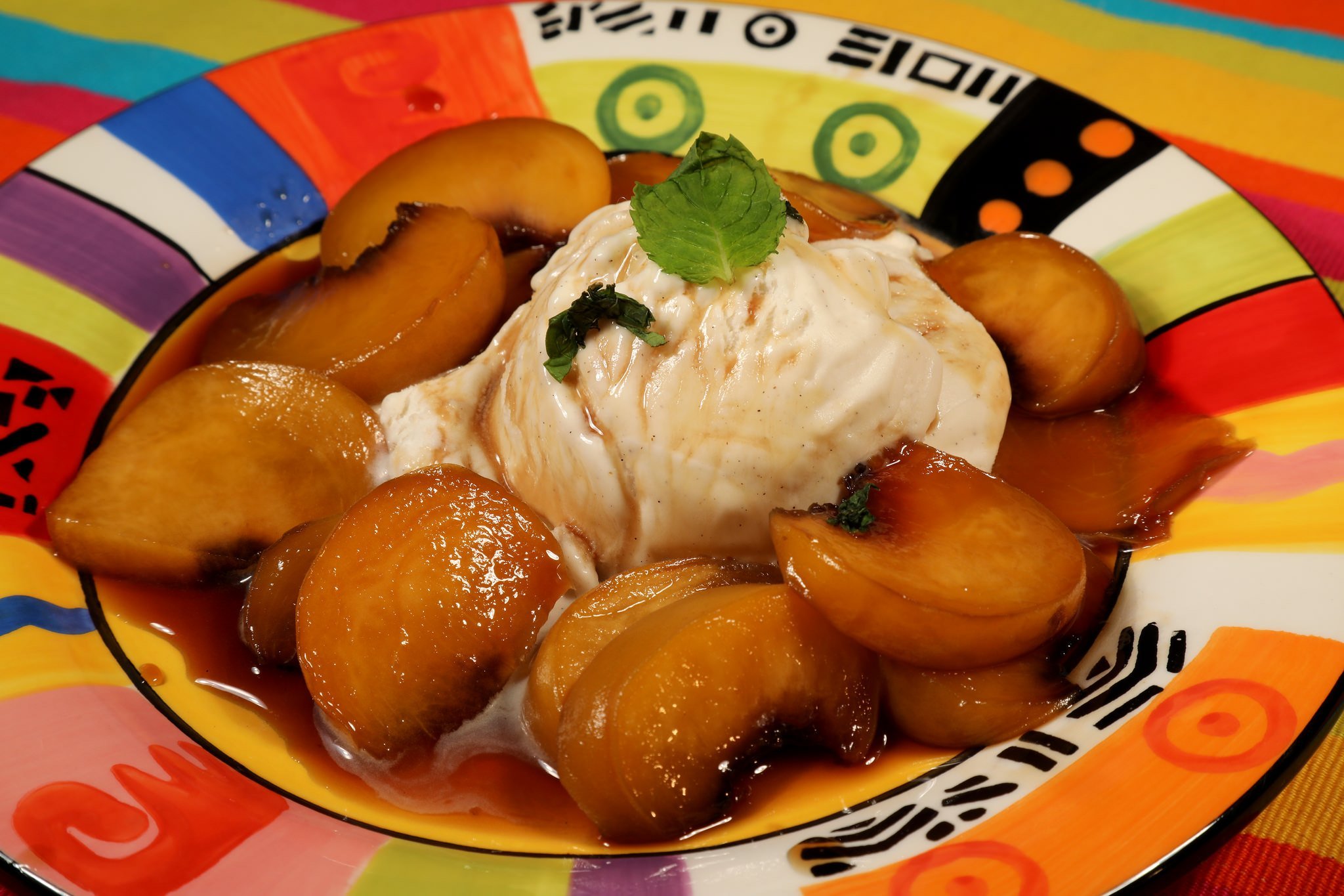 brown sugar peaches topped with ice cream and mint sprig on a colorful plate