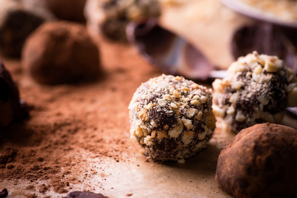 Assorted dark chocolate truffles with cocoa powder, biscuit and chopped hazelnuts over baking paper, selective focus, close up