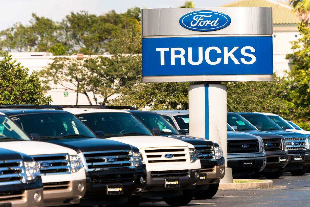 Line of Ford trucks at a car dealership with Ford sign