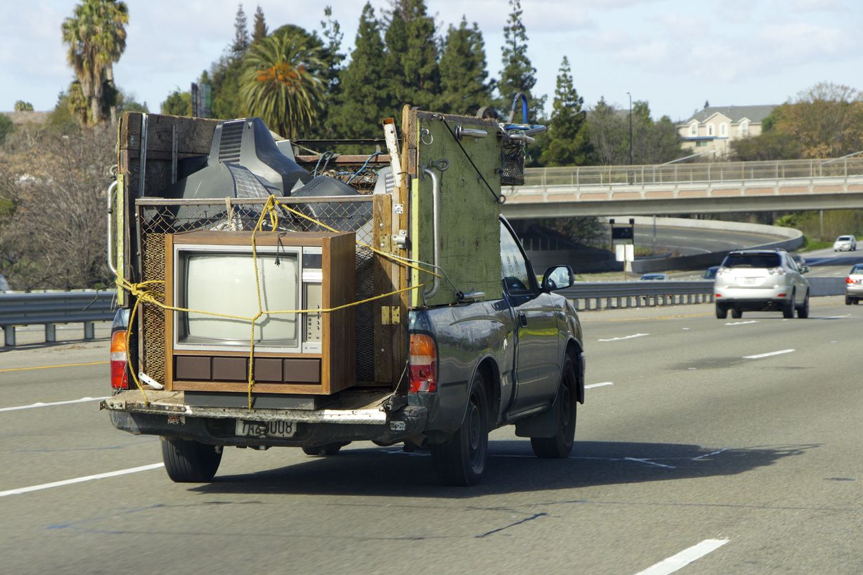Old pickup truck with old TV tied down in truck bed goes on the highway