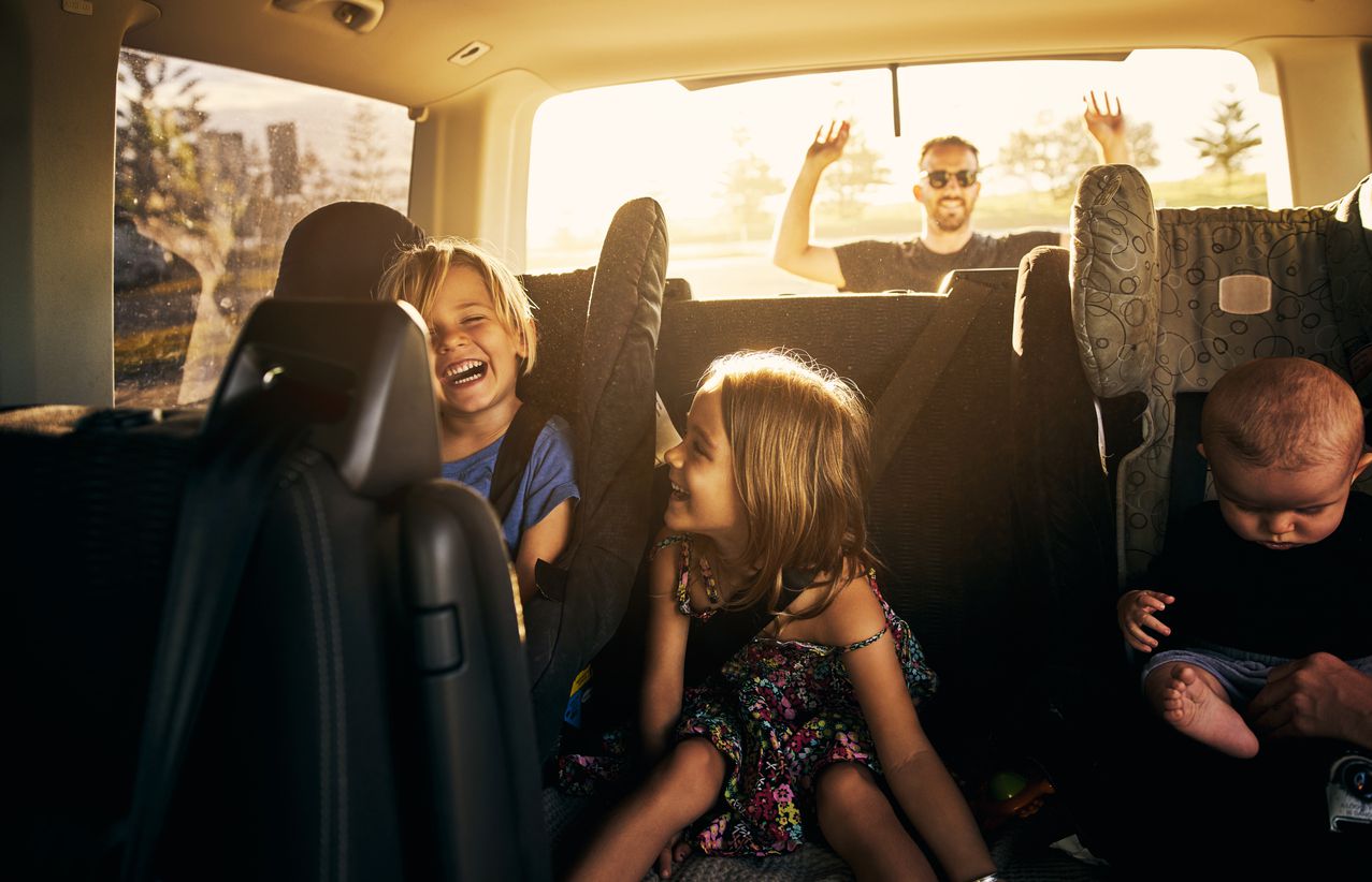 Three children in carseats in back seat of car and the dad closing the trunk- full car