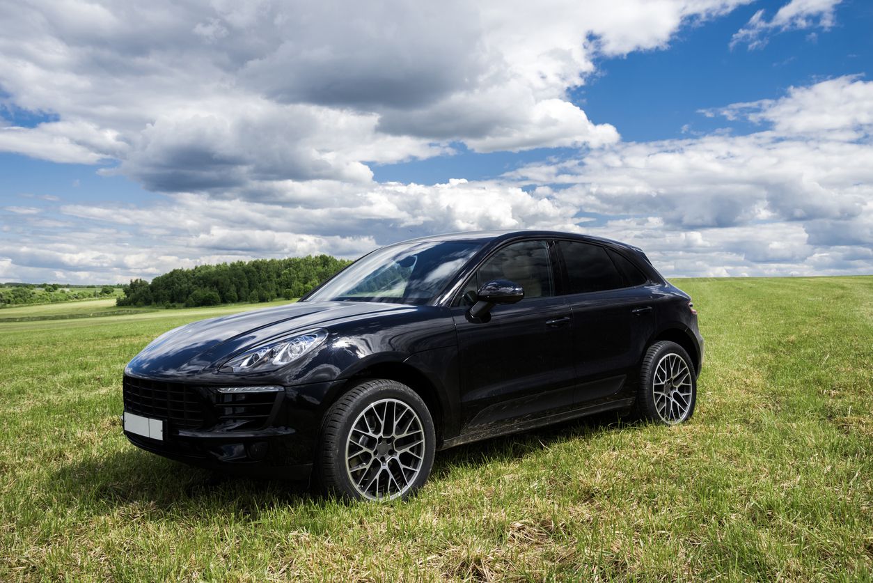 A black Porsche Macan is parked on a fresh green spring grass