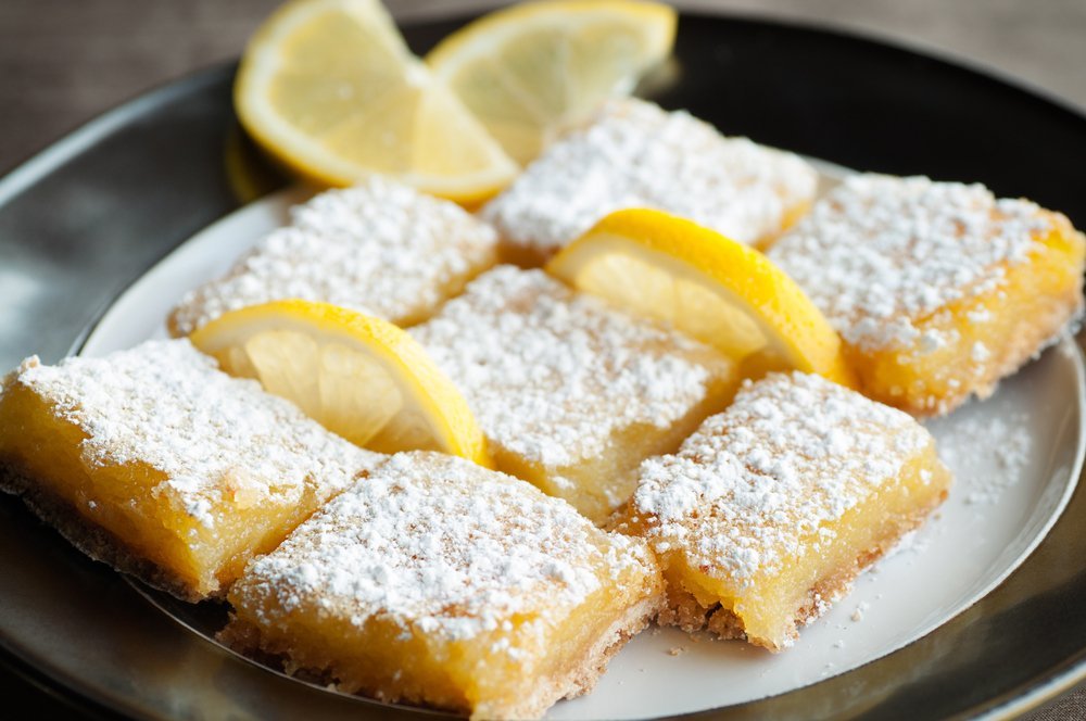 plate of lemon bars topped with powdered sugar and fresh lemon slices
