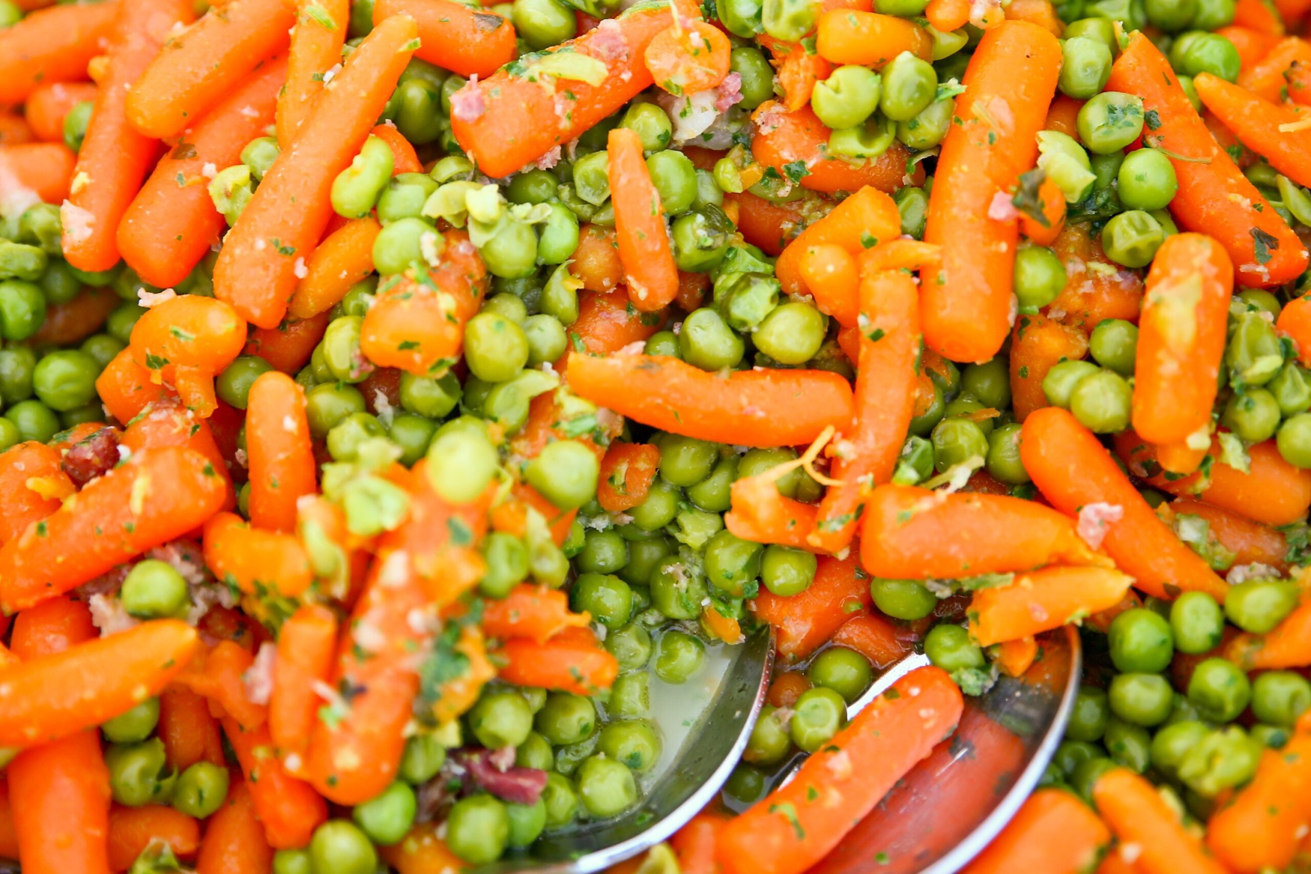 closeup of peas and carrots dish with serving spoon