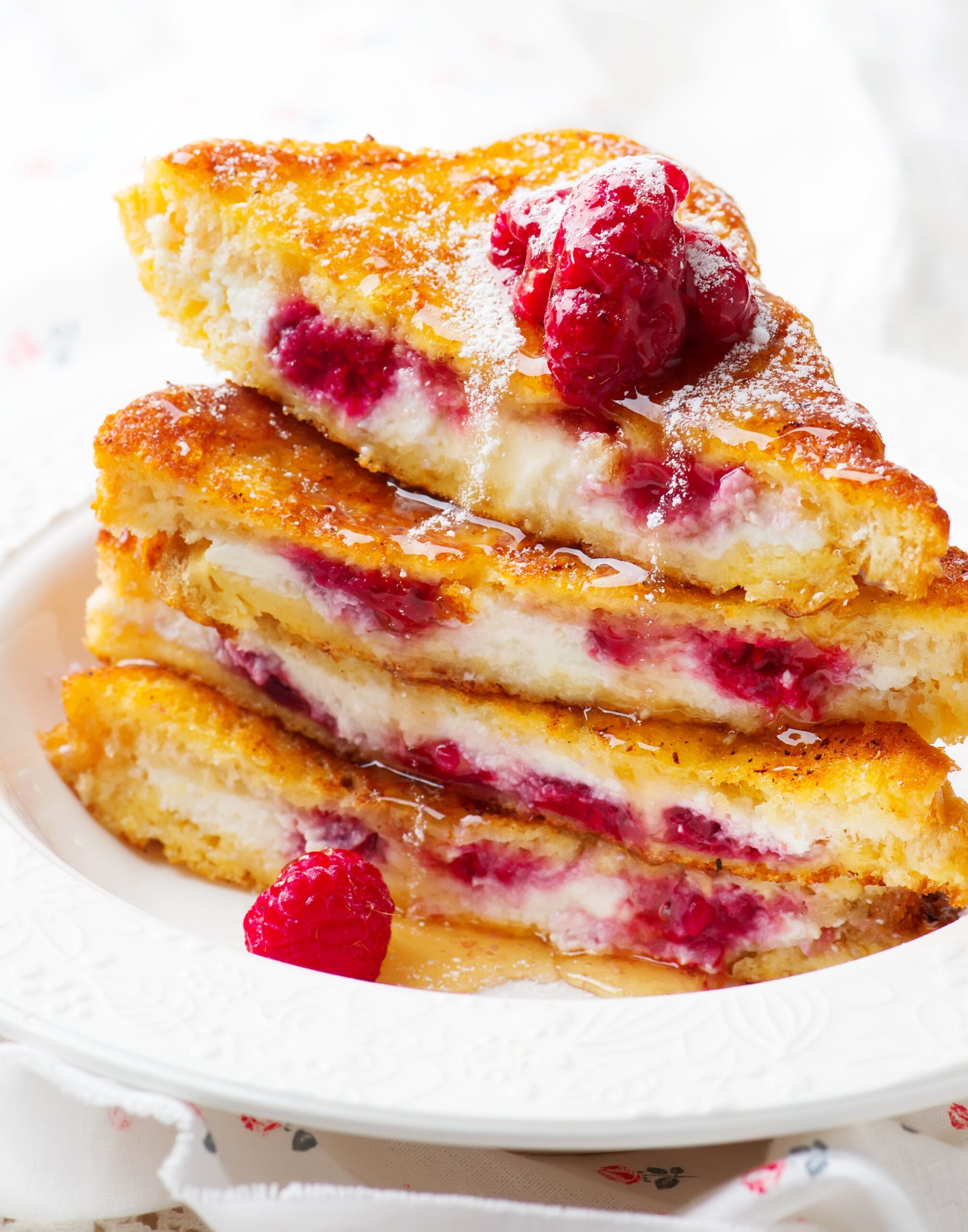plate with 3 slices of stuffed french toast with raspberries stacked on top of each other