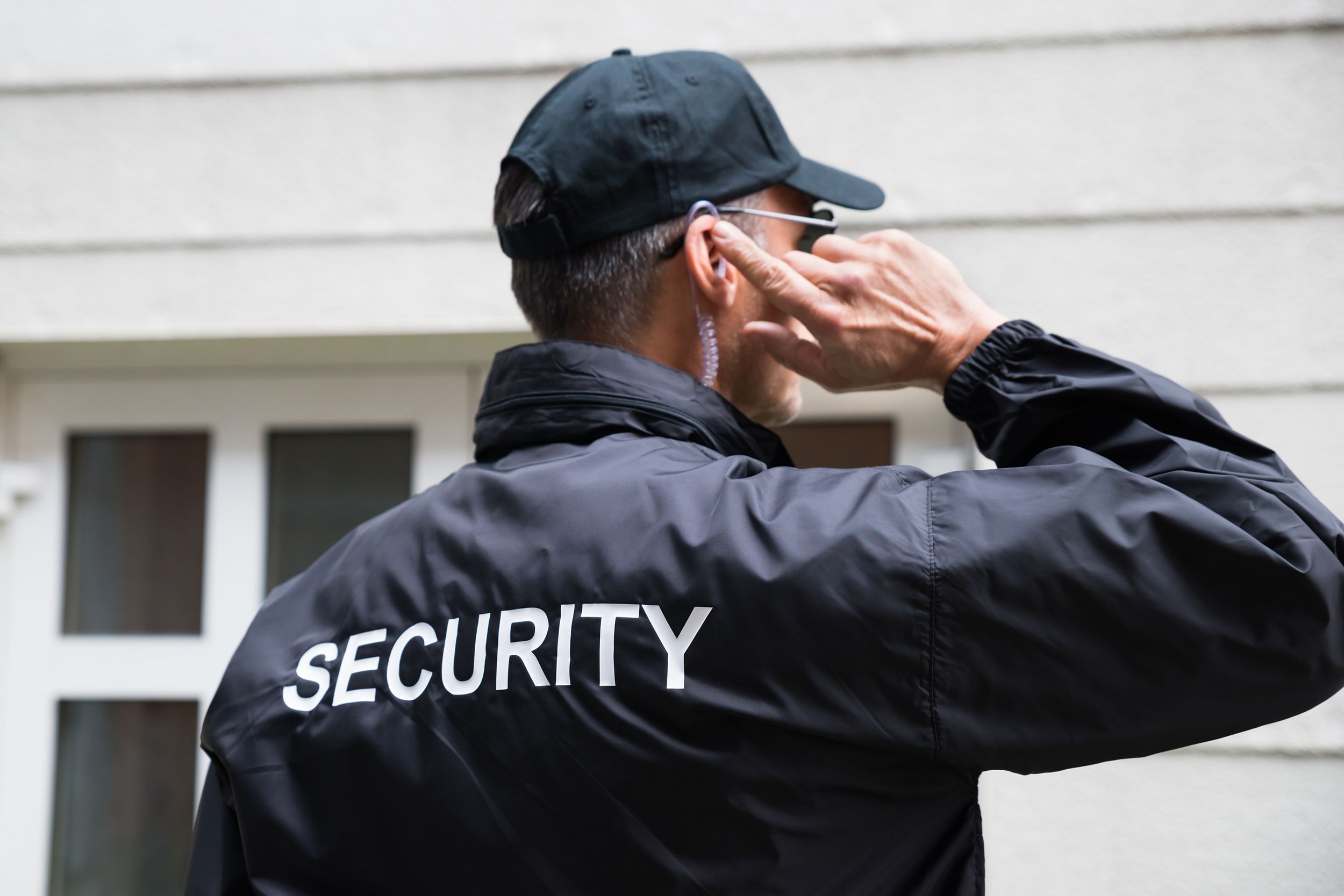 security guard listening to earpiece against building