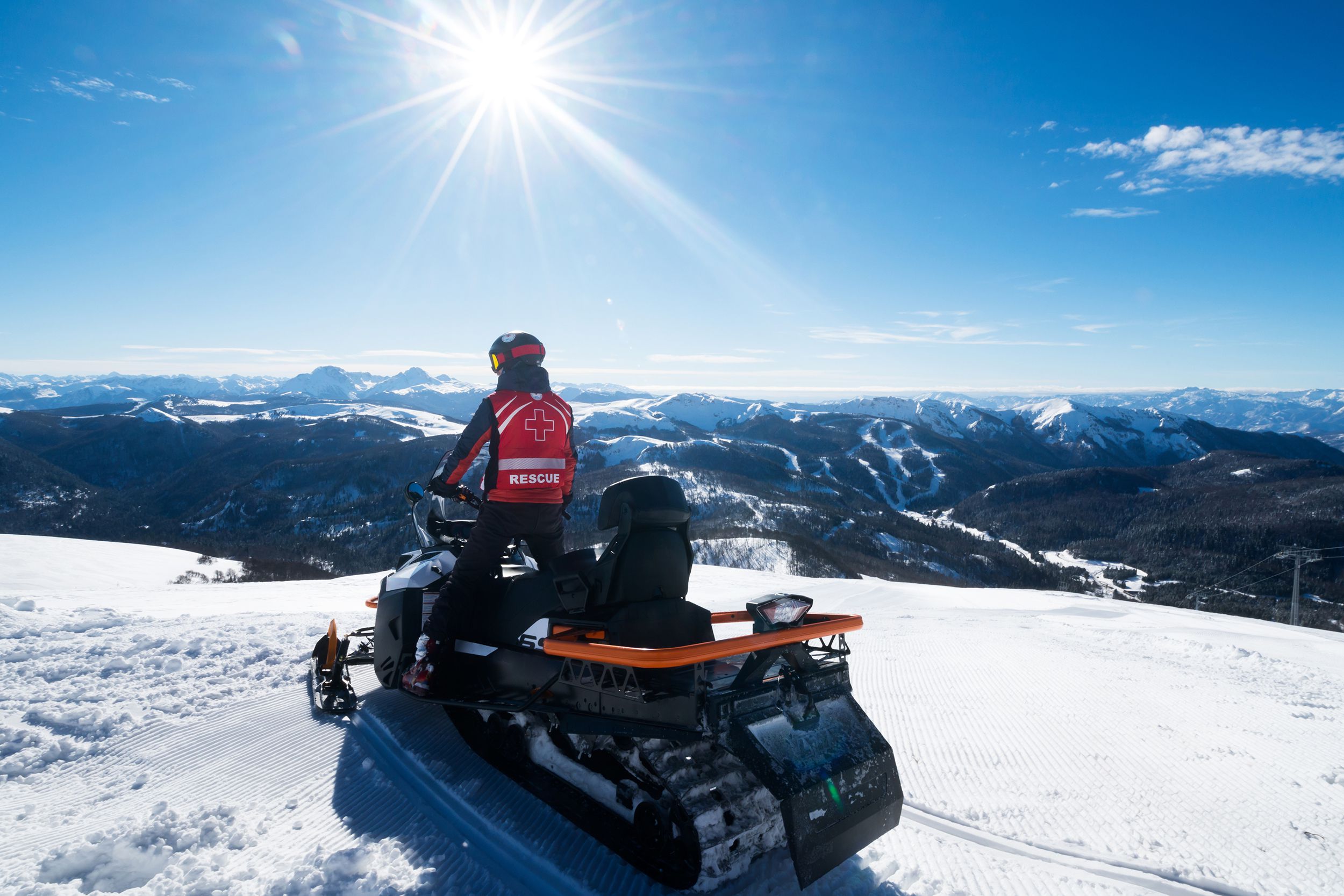 mountain rescue-man standing on his snow sled on a top of the mountain and enjoying a panoramic view