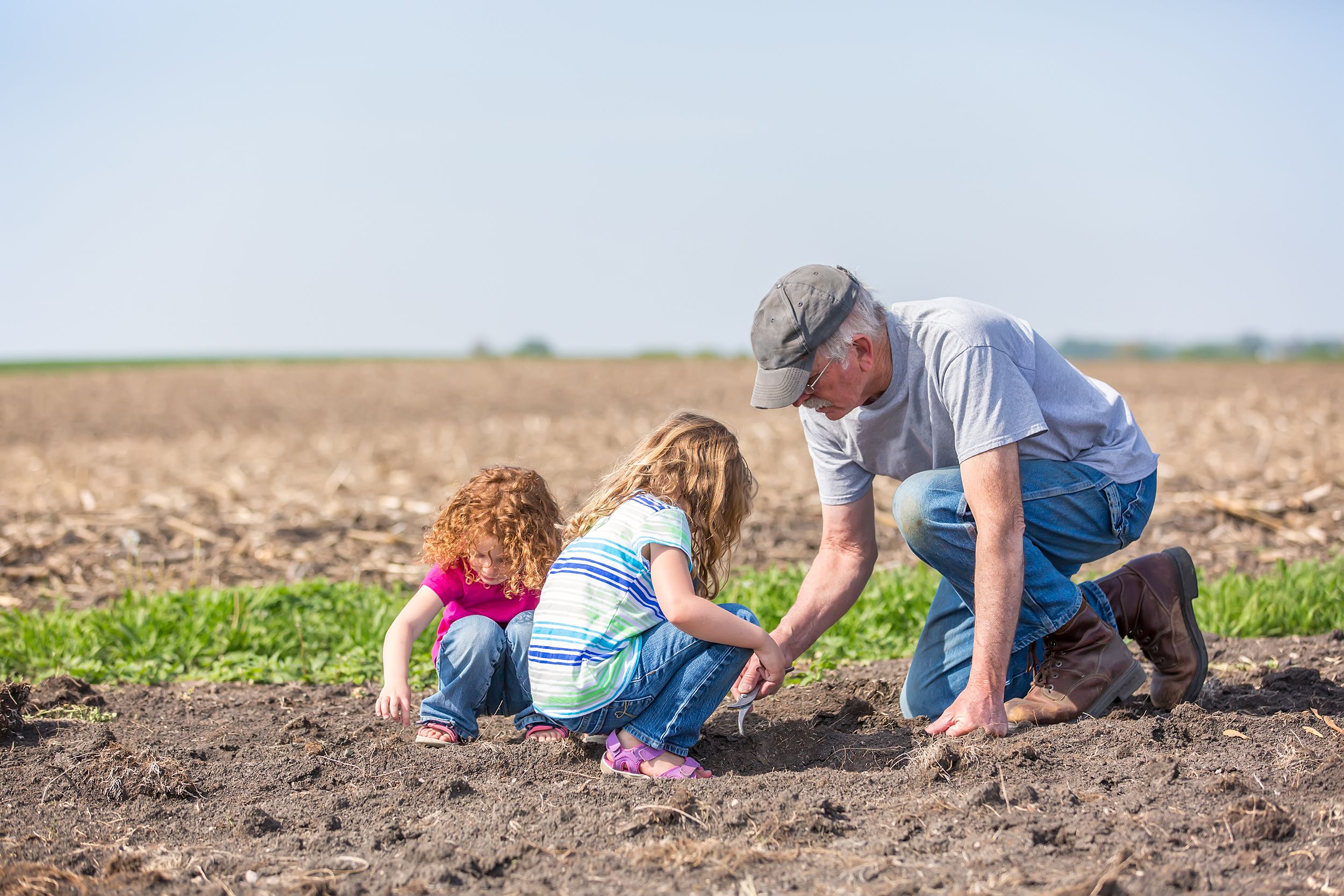 granddaughters and grandpa checking field for growing soybeans