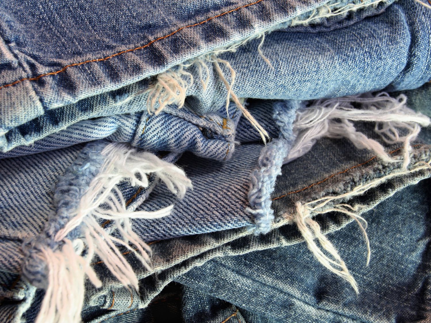 An abstract pile of several different pairs of ragged old blue jeans ready to be recycled.