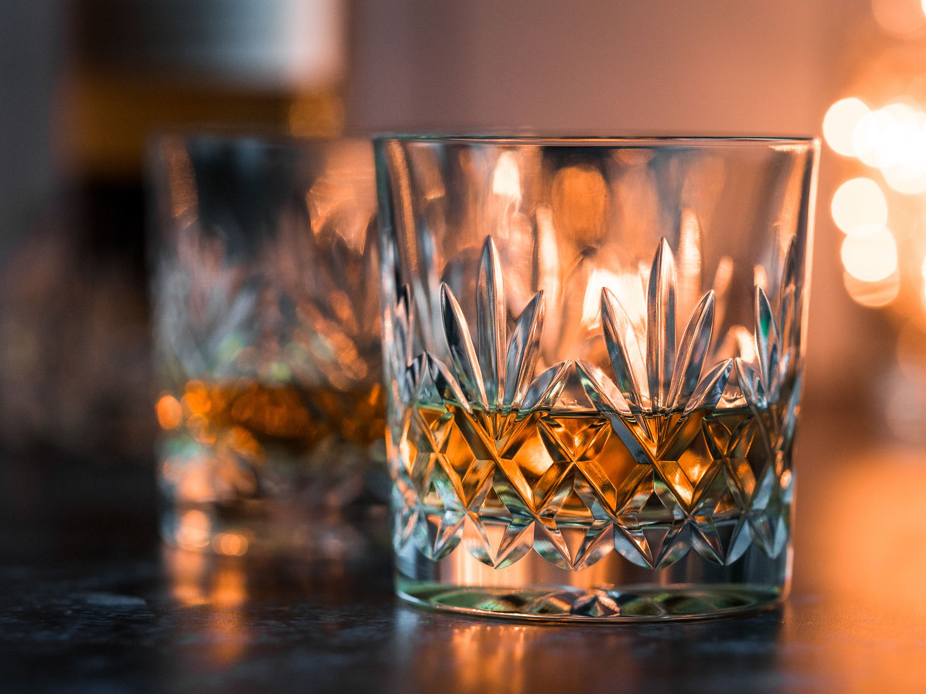 Close up color image depicting two fine crystal glasses of malt whisky on a white wooden surface. The glasses of whisky are surrounded by whisky paraphernalia such as a glass decanter and a hip flask. Room for copy space.