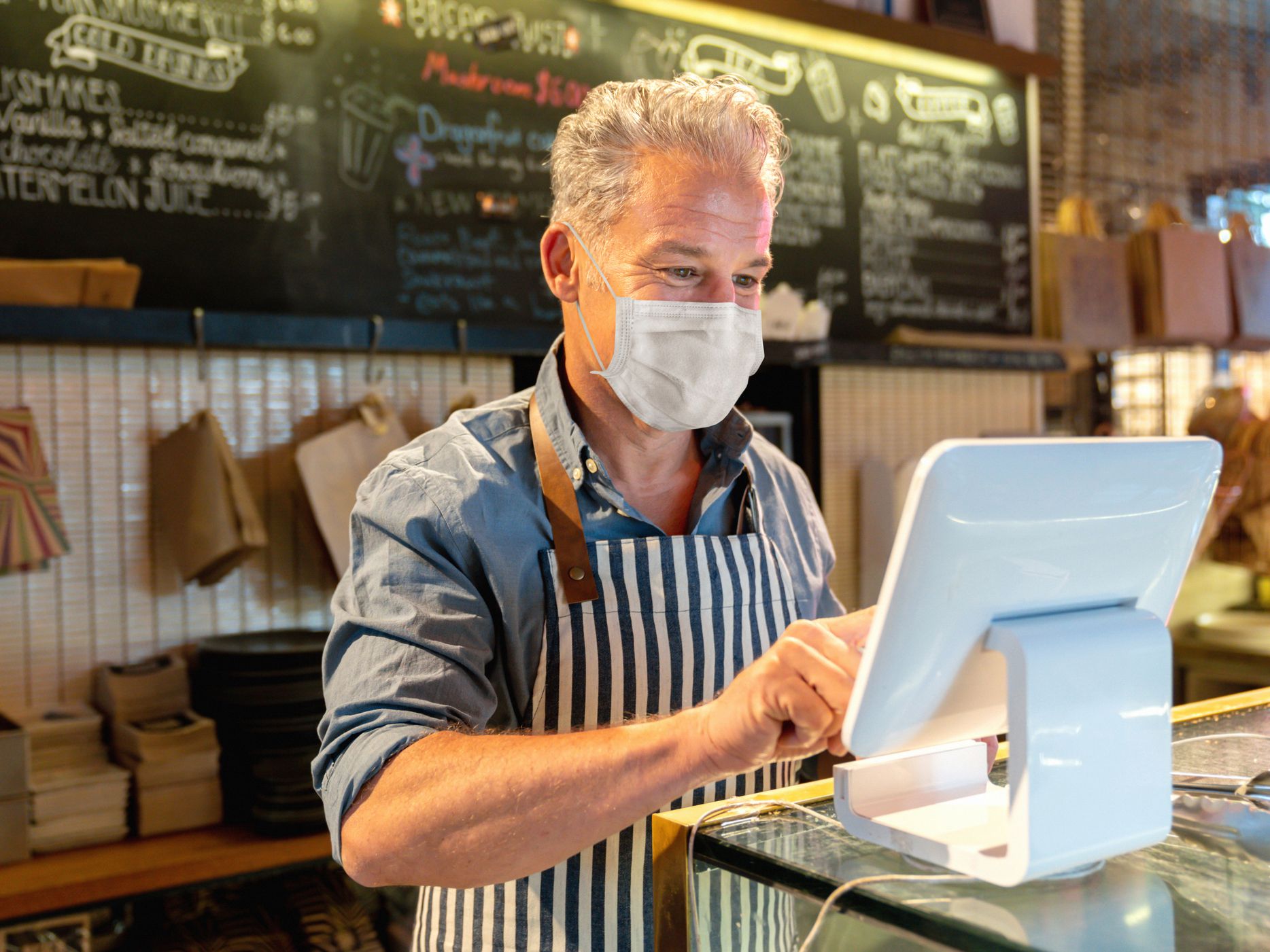 Portrait of a happy business manager working at a cafe and placing an order at the till on the computer and wearing a facemask