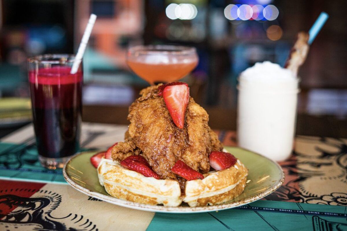 fried chicken on waffle on plate with three cocktails in the background on bar counter at Punch Bowl Social, San Diego, California