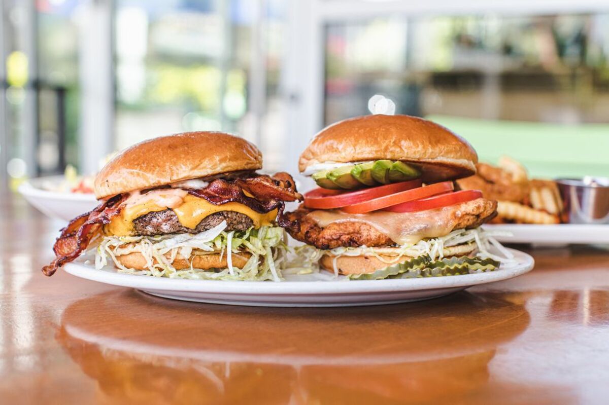 two loaded hamburgers on plate with fries and sides on plates in the background at Zinburger, Phoenix, Arizona