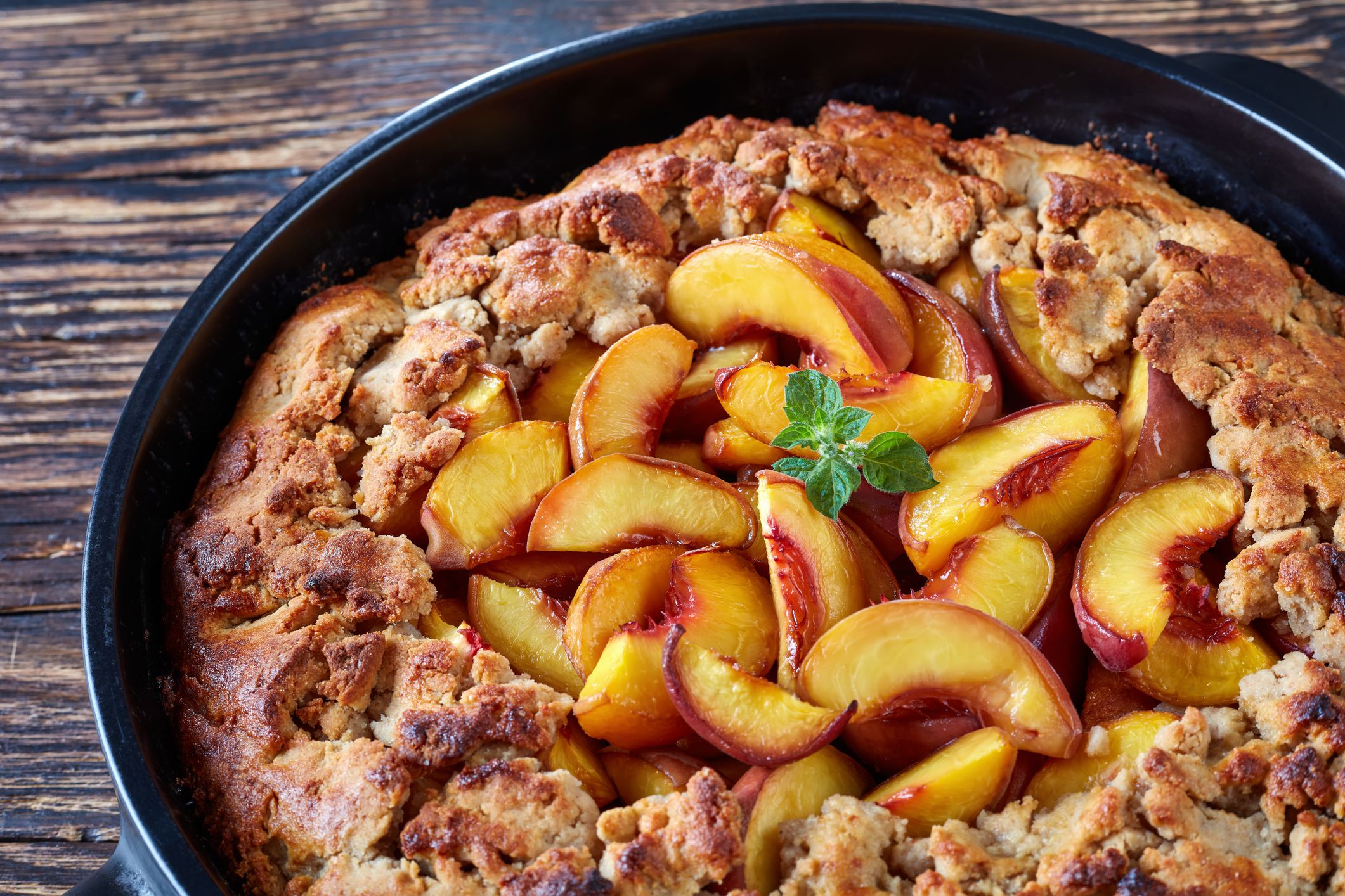 Close up of delicious southern dessert peach cobbler baked in a black dish, presented on old wooden table