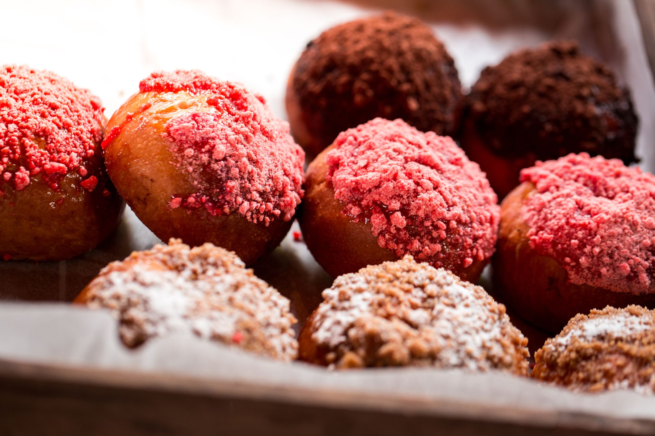Close up macro color image depicting an overhead view of freshly made donuts topped with pink frosting on display and for sale at a food market. Room for copy space.