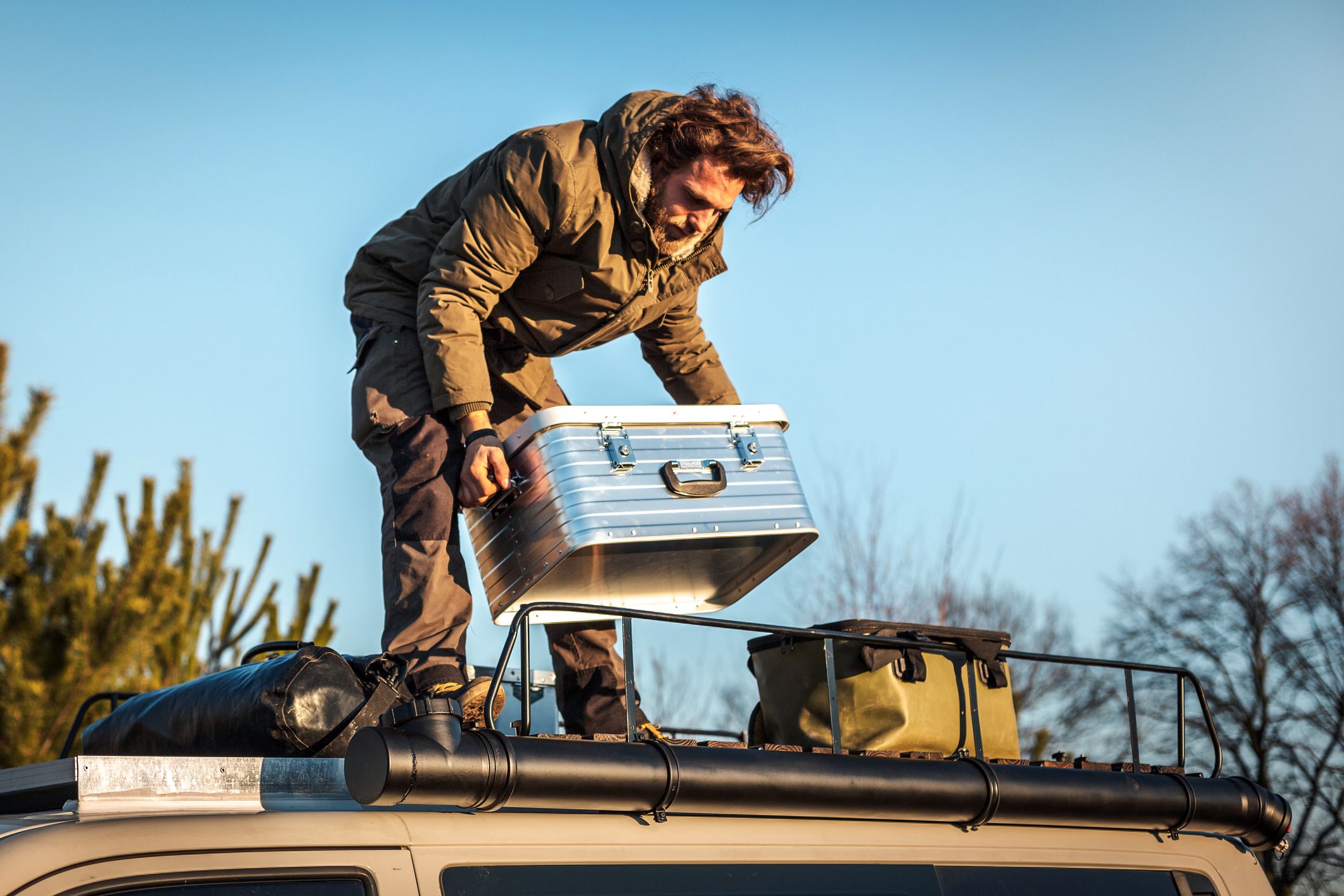 man lifting a metal box from the roof rack of a van