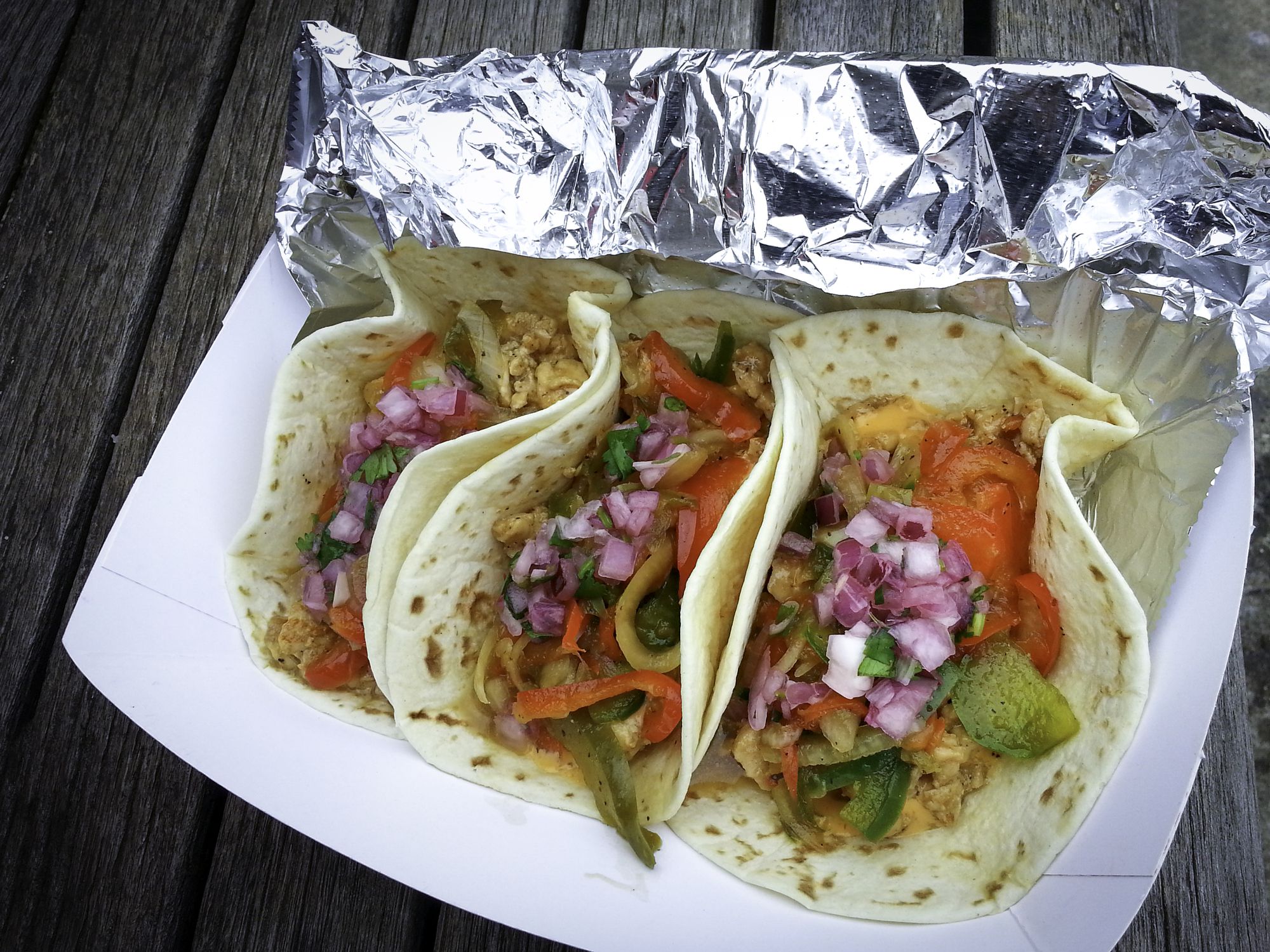 Delicious Takeout Tacos With Chicken, Lettuce, Tomato, and Onions, on old wooden table in the public parking lot
