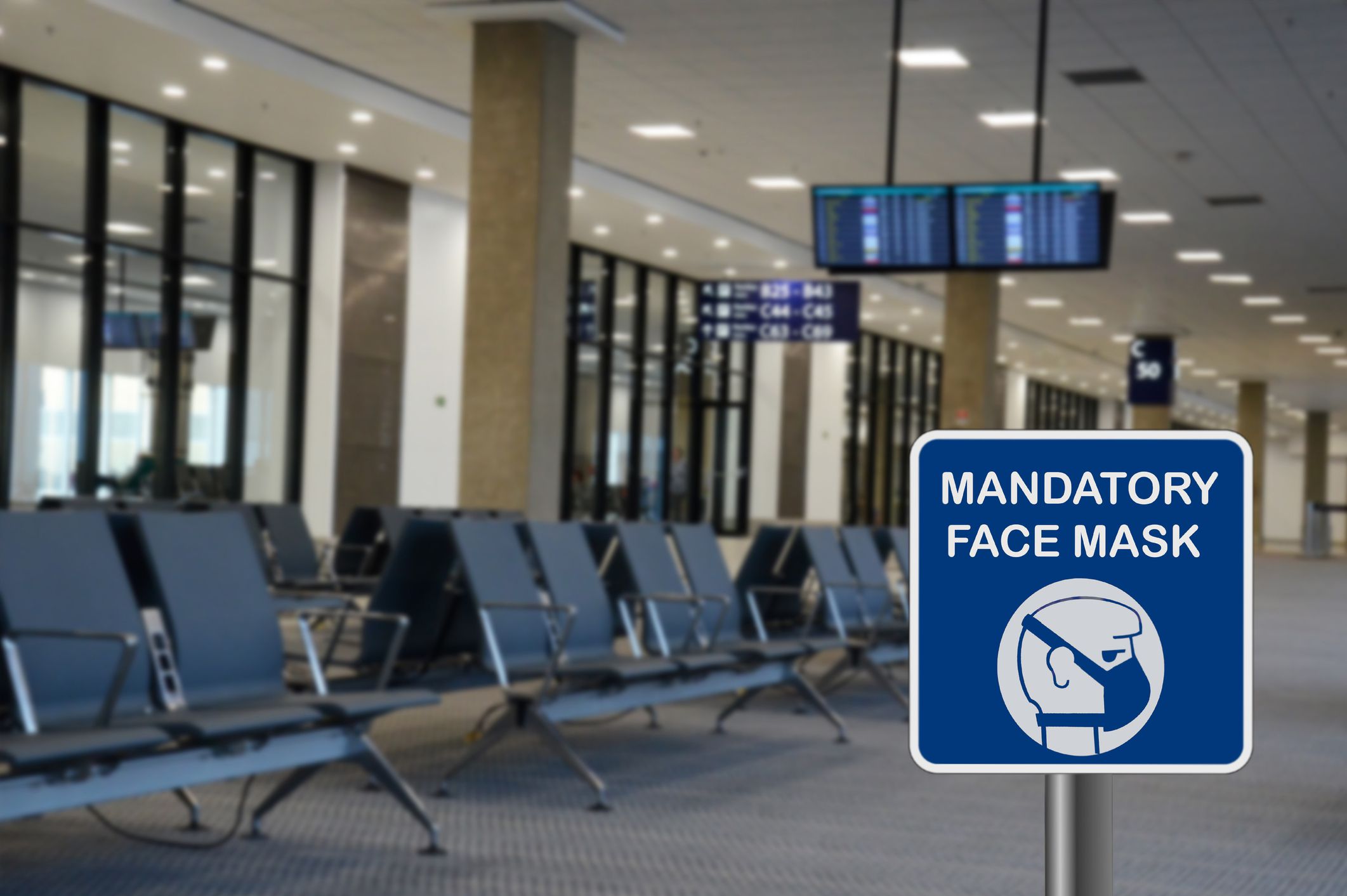 Blue sign warning of that face mask is mandatory due to Covid-19 or coronavirus in airport, with in a purposely blurred background an empty airport waiting room
