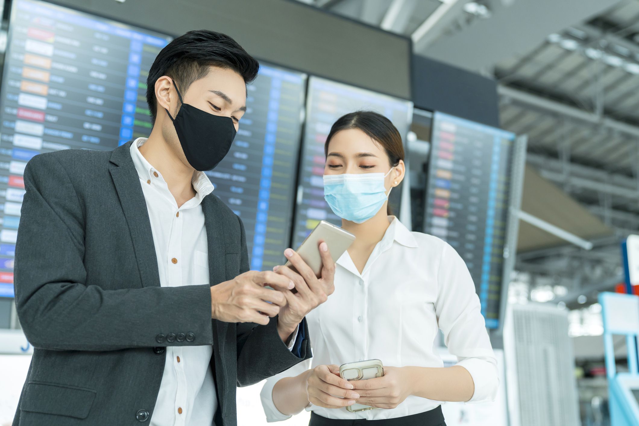 two asian businessman and businesswoman with face mask protection in international airport terminal conversation near information board business concept