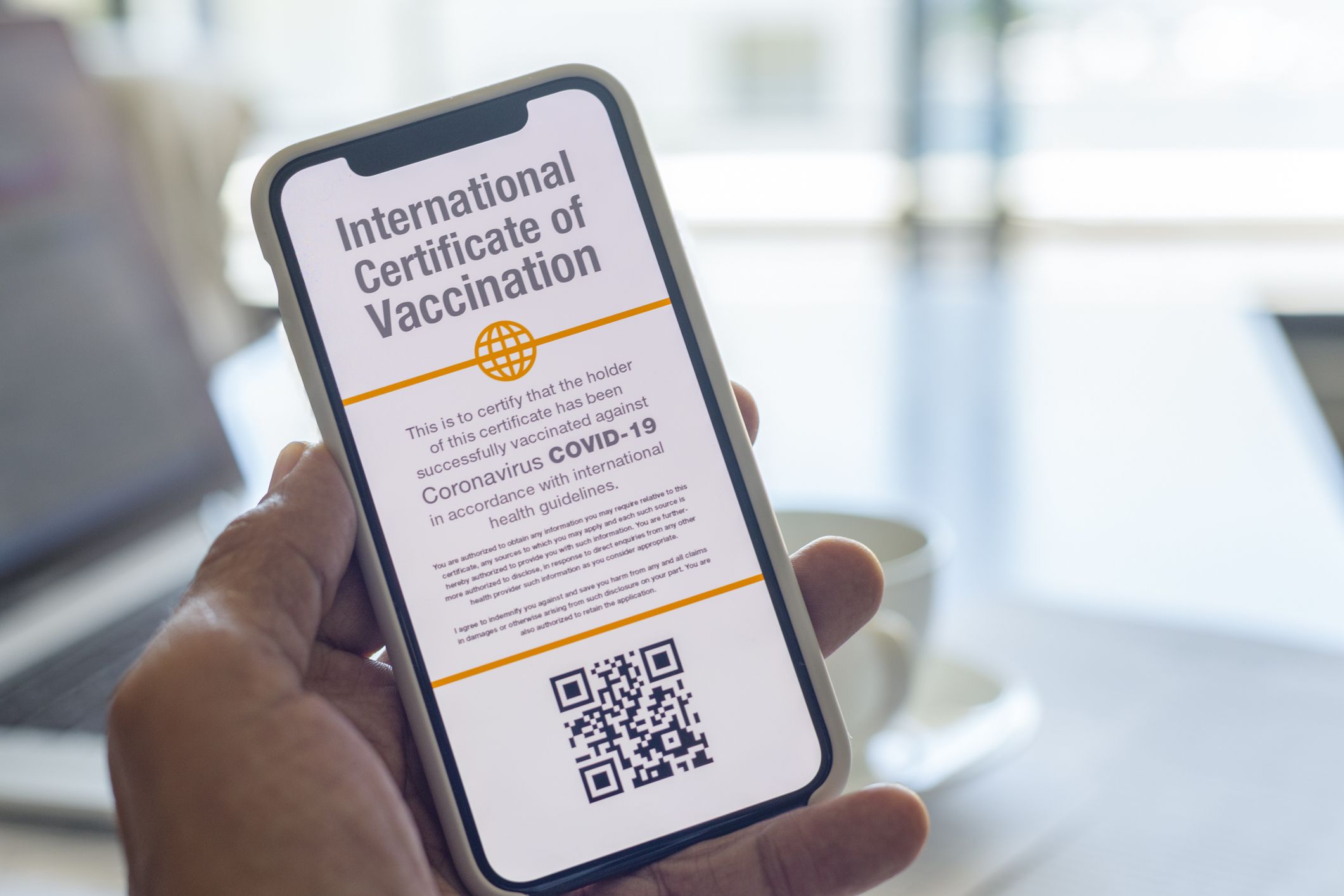 Digital International Certificate of Covid-19 Vaccination. The certificate indicates that the holder has been vaccinated against Coronavirus Covid-19. There is a coffee cup and laptop computer in the background.