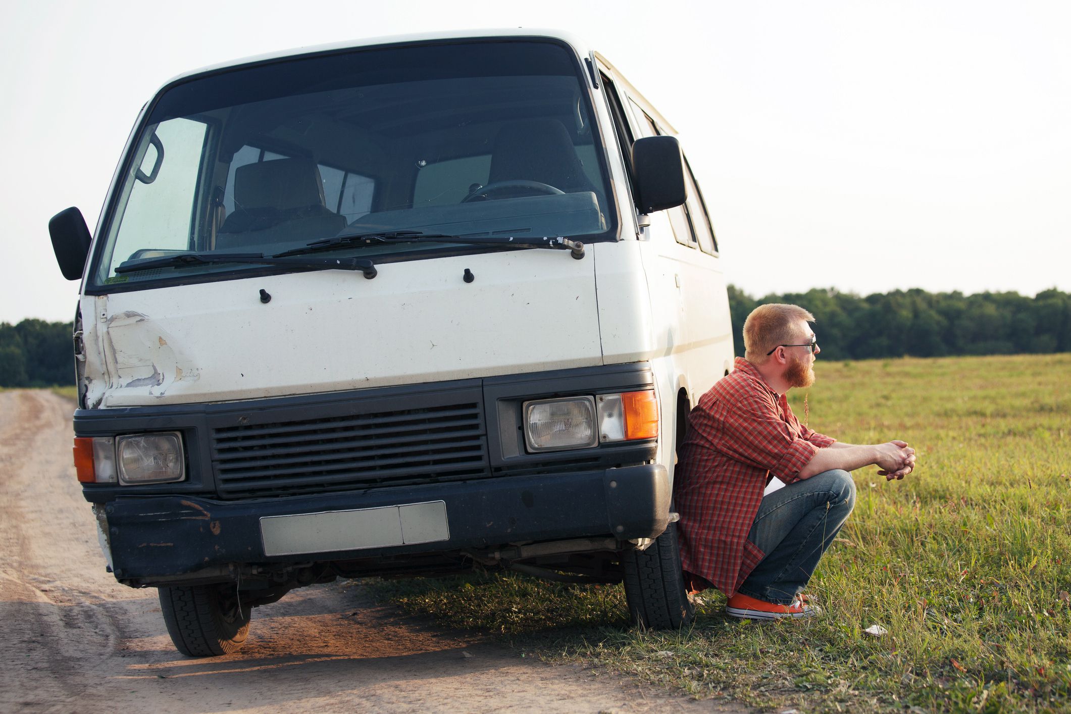 man crouching next to broken down van on side of road