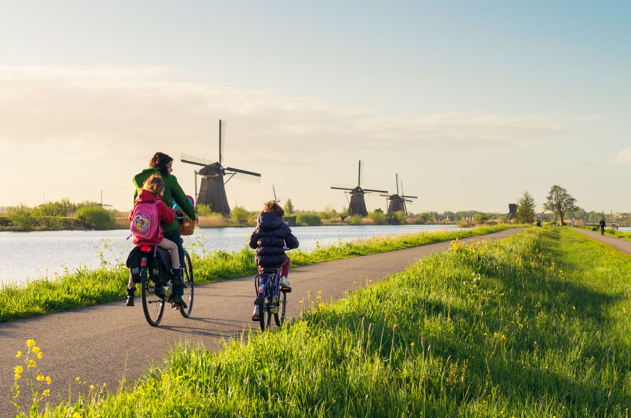 Kinderdijk, The Netherlands - Rear view of a woman and two children as they cycle along a canal path lined with traditional Dutch windmills.