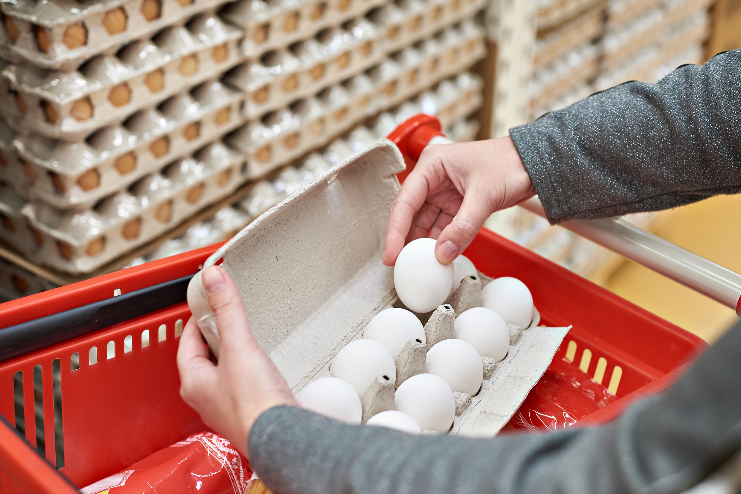 hands with packages of white eggs in store
